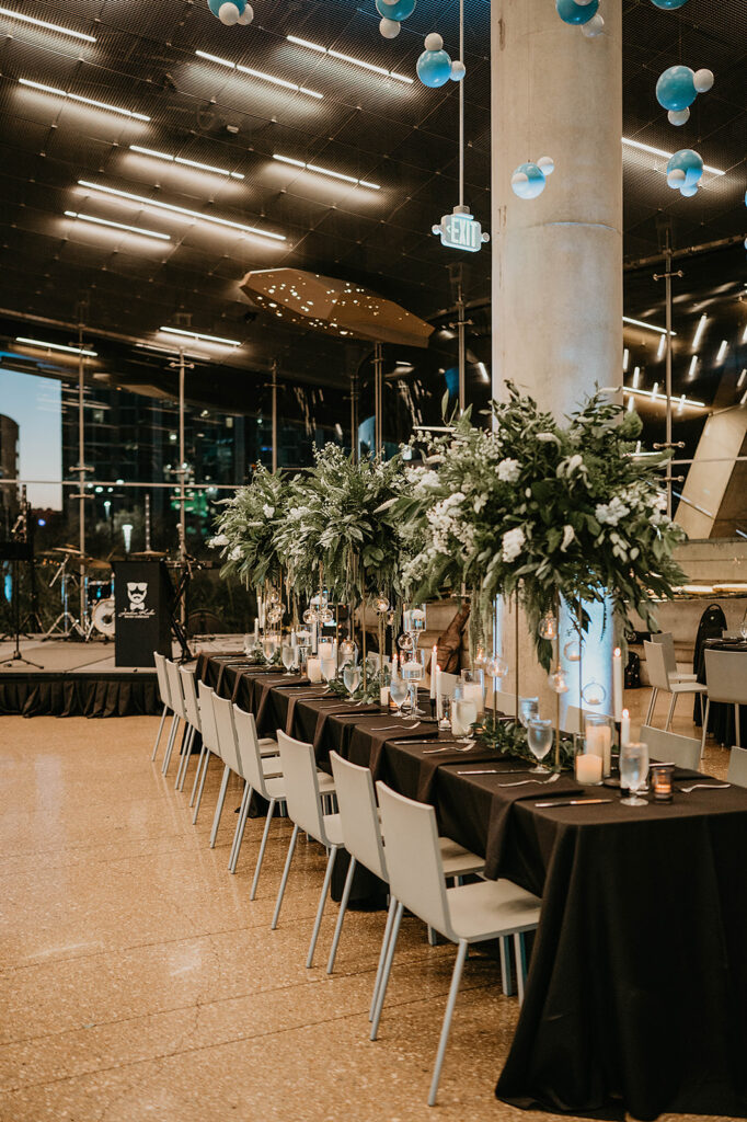 Long banquet tables with tall greenery centerpieces set for an evening event